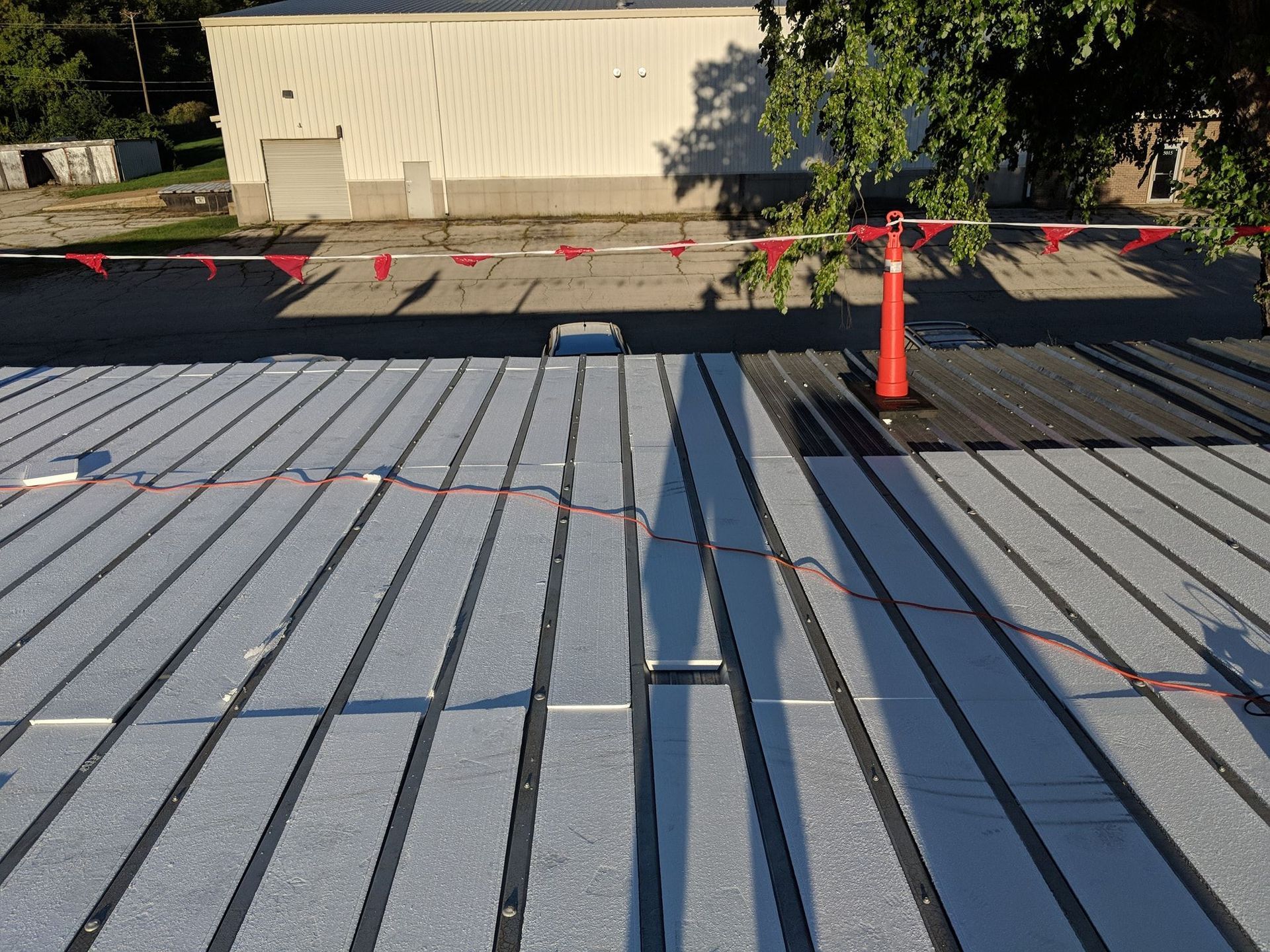 A rooftop view of gray insulation panels installed in rows with dark structural ridges, sectioned off by orange cones.