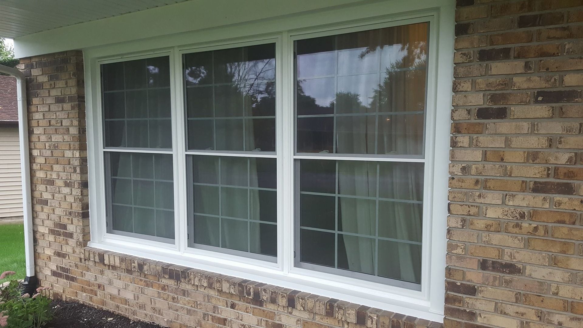 A white-framed triple-pane window with a grid pattern on a beige brick house exterior.