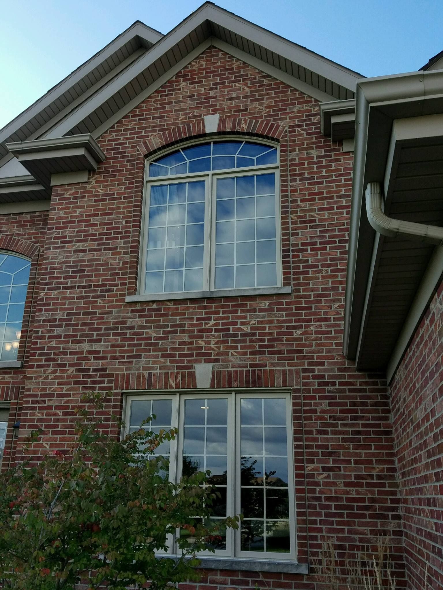 Two stacked windows with a grid pattern set into a reddish-brown brick wall of a house exterior.