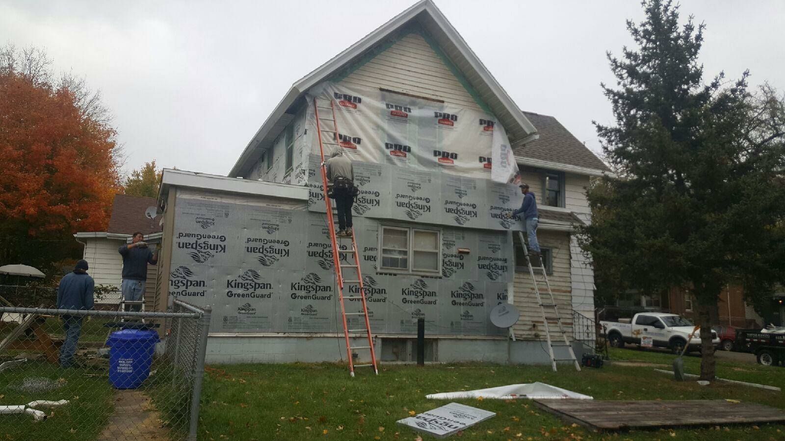 Workers in safety gear install weather-resistant wrap on the side of a two-story residential house.