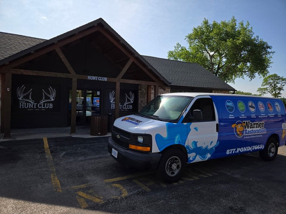 A Manning Brothers service van parked in front of a Hunt Club building on a sunny day.