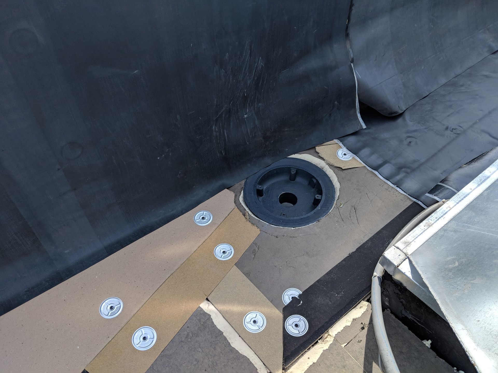 A black roof drain installed in a flat roof surface, surrounded by beige insulation boards secured with metal washers.