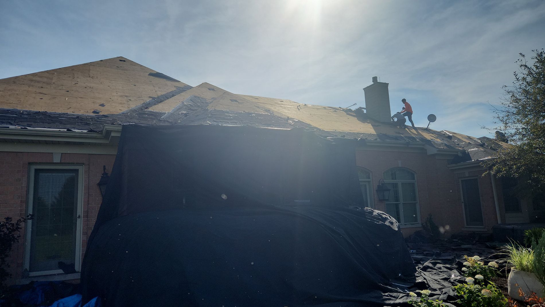 Workers on a roof during a sunny day as they remove old shingles from a house.