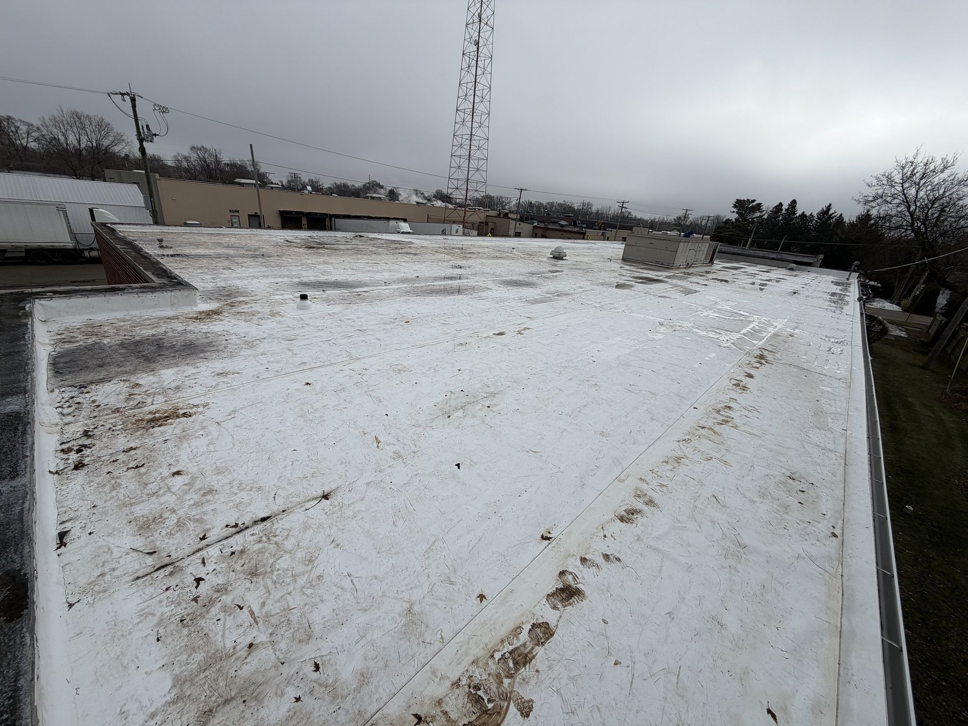 A wide-angle view of a weathered white flat roof on a commercial building under a cloudy sky.