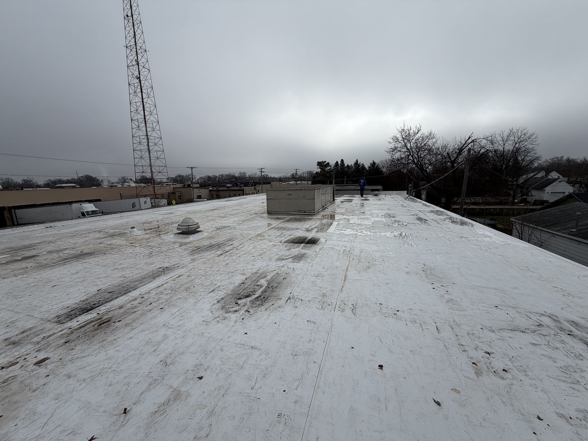 A wide view of a flat, white rooftop with some dirt and a rectangular vent, under a cloudy, overcast sky.