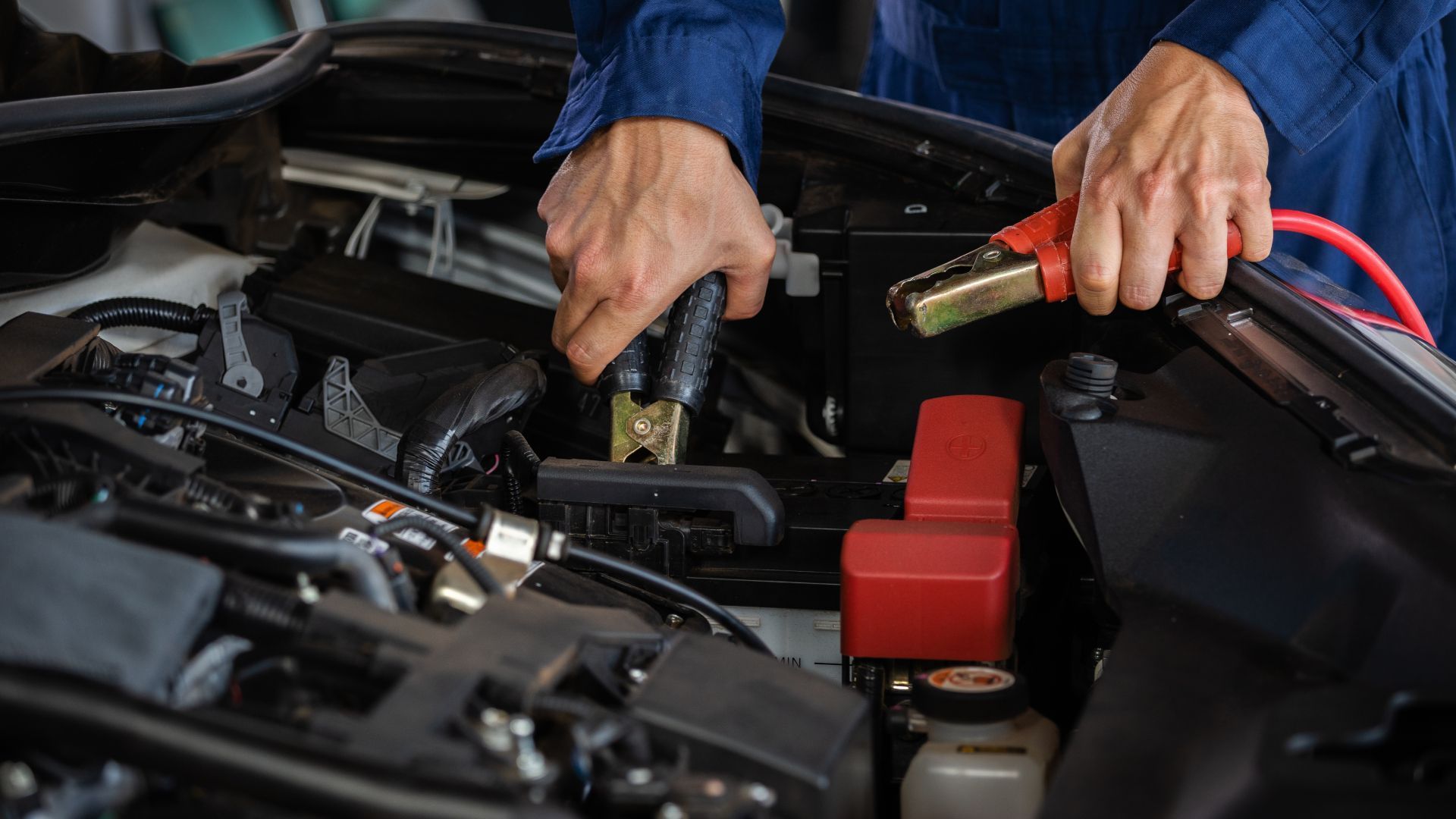 Hands using a jumper cable to charge a car battery in an open engine bay