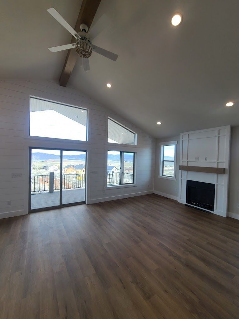 Bright empty living room with vaulted ceiling, ceiling fan, fireplace, and large windows overlooking a balcony