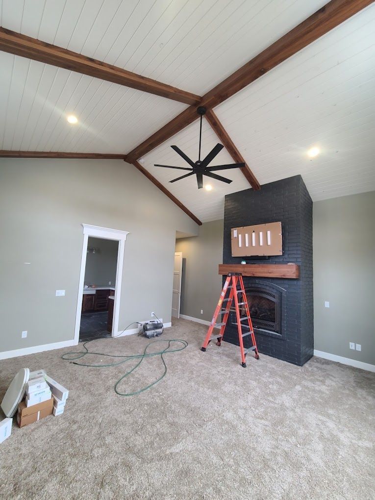Living room under renovation with vaulted ceiling, fireplace, ladder, and construction tools on carpet.