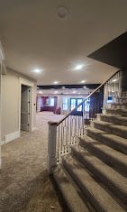 Carpeted indoor staircase with white railing in a well-lit lobby or hallway.