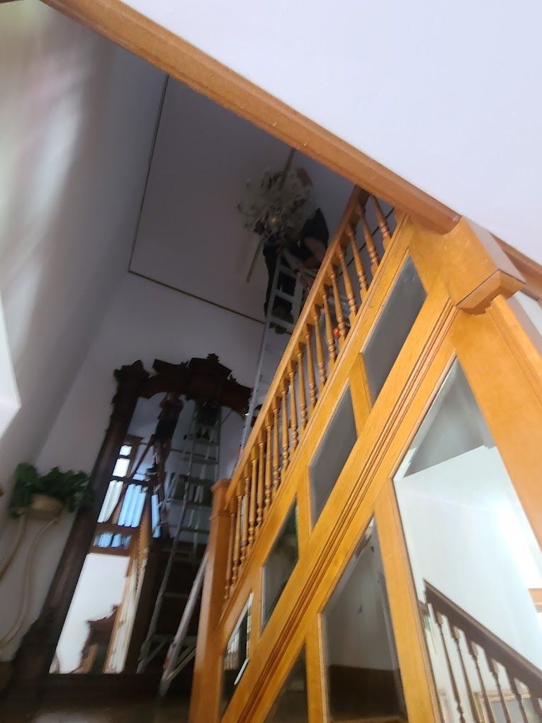 Wooden staircase with railing in a bright indoor entryway, viewed upward toward a tall mirror and plant.