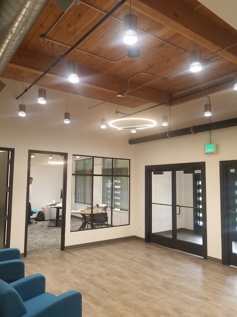 Empty modern office lounge with wood ceiling, glass walls, blue chairs, and bright pendant lights