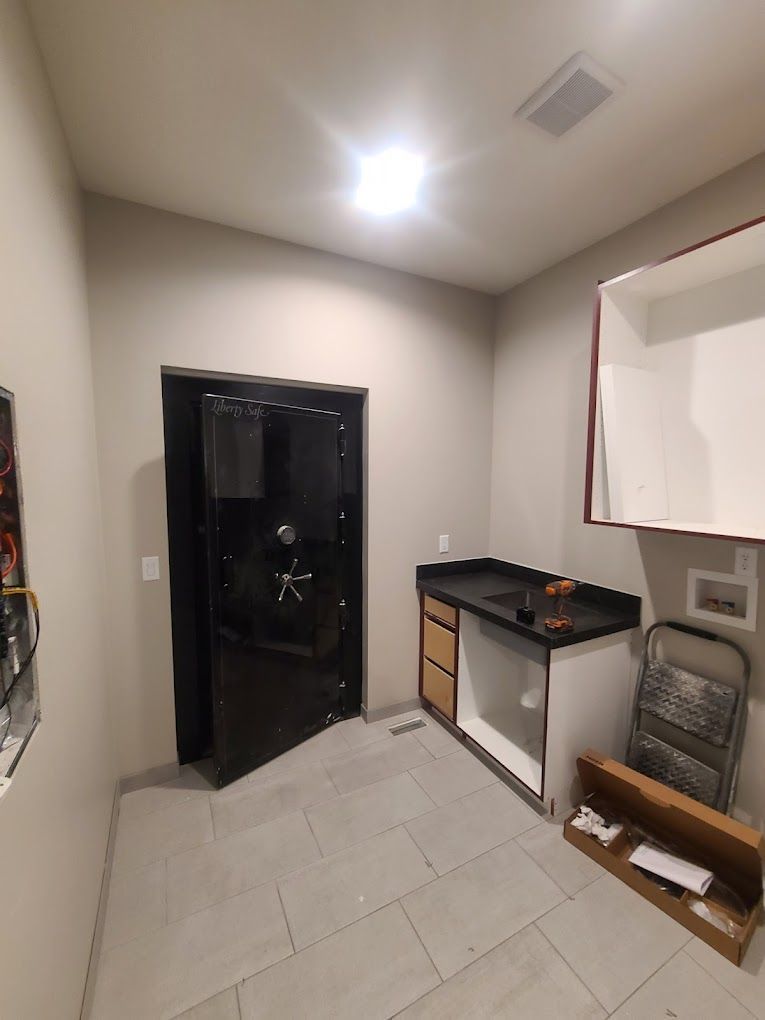 Small utility room with black door, white tile floor, countertop cabinet, and open boxes near the wall.