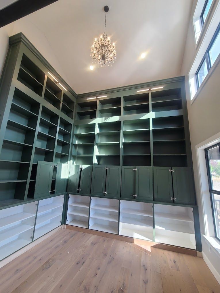 Built-in dark green shelving in a bright room with wood floor and chandelier