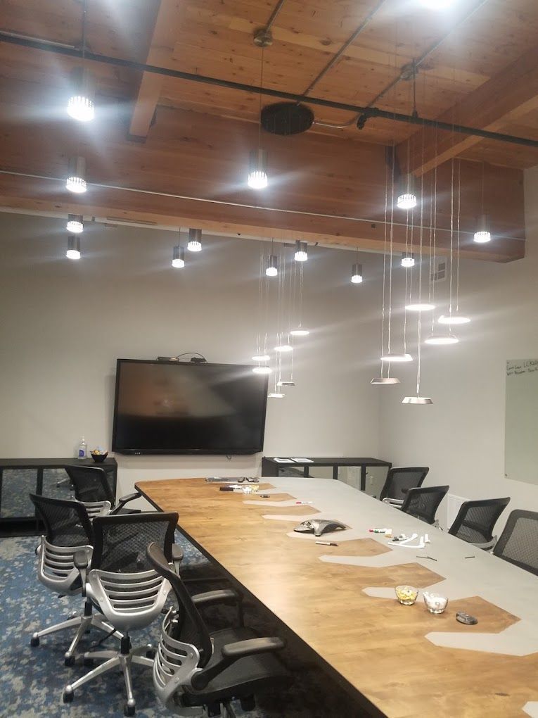 Conference room with long wooden table, rolling chairs, wall-mounted TV, and hanging pendant lights