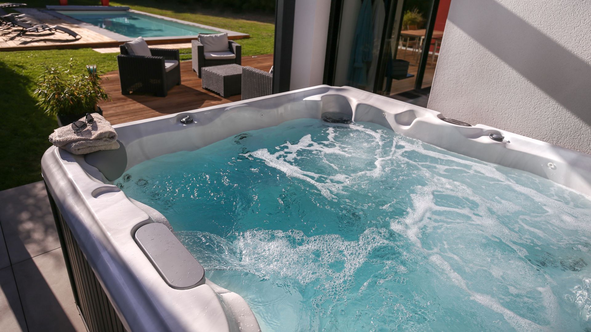 Outdoor hot tub with bubbling blue water on a patio overlooking a pool and yard