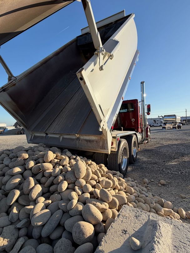 A dump truck is loading gravel into the back of it.