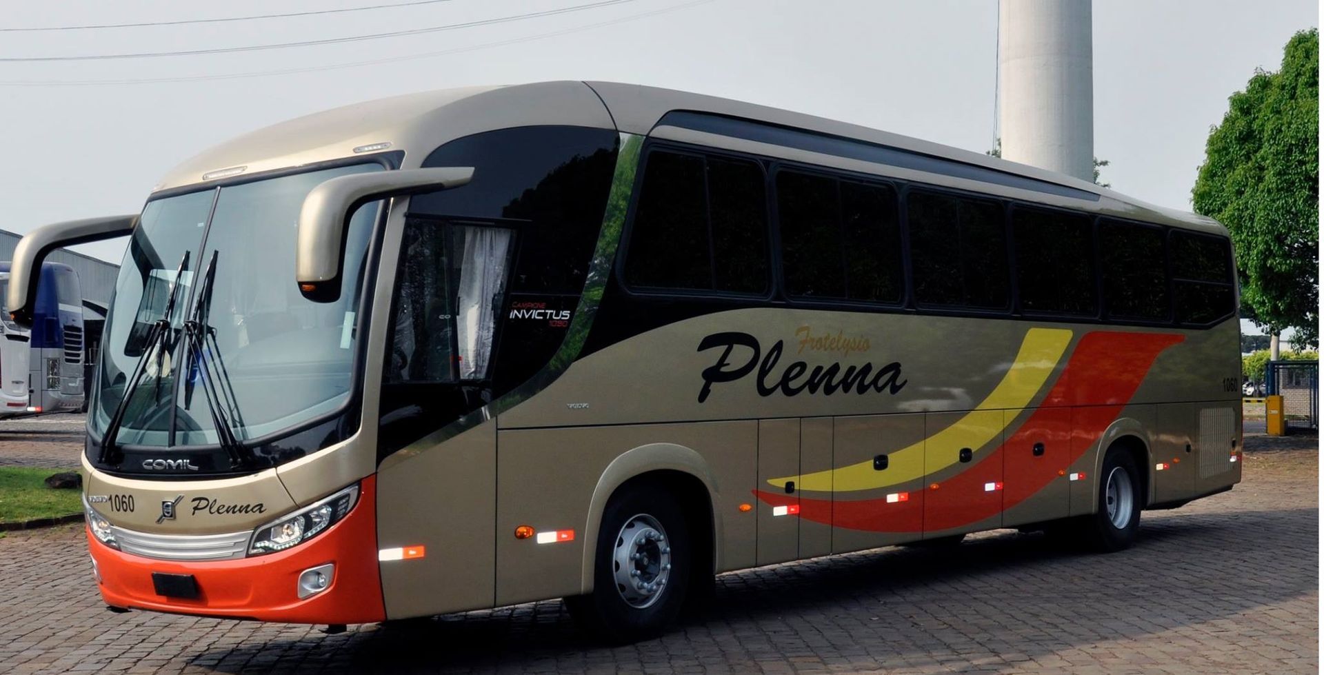 Ônibus de turismo prateado e laranja estacionado ao ar livre com o logotipo