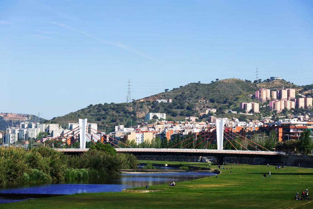 Parque verdejante e lago com vista para o horizonte da cidade e a encosta sob um céu azul límpido.