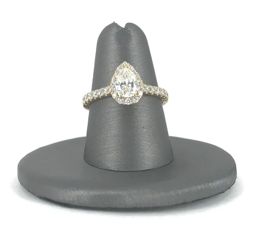 A pear shaped diamond ring is sitting on a gray ring holder