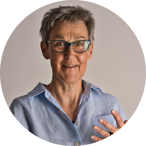 Foto Noemi Koch - Noemi steht vor einem neutralen Hintergrund, sie trägt ein Denimhemd. Noemi hat kurze Haare und trägt eine Brille.