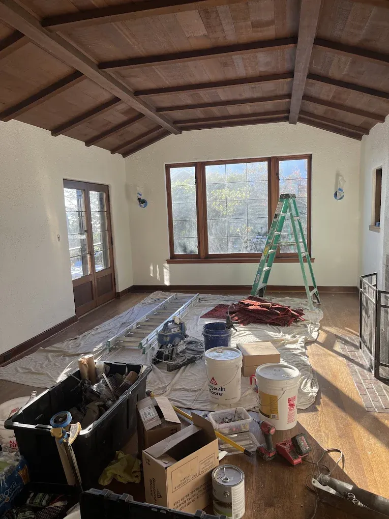 A living room with a ladder and buckets of paint on the floor.