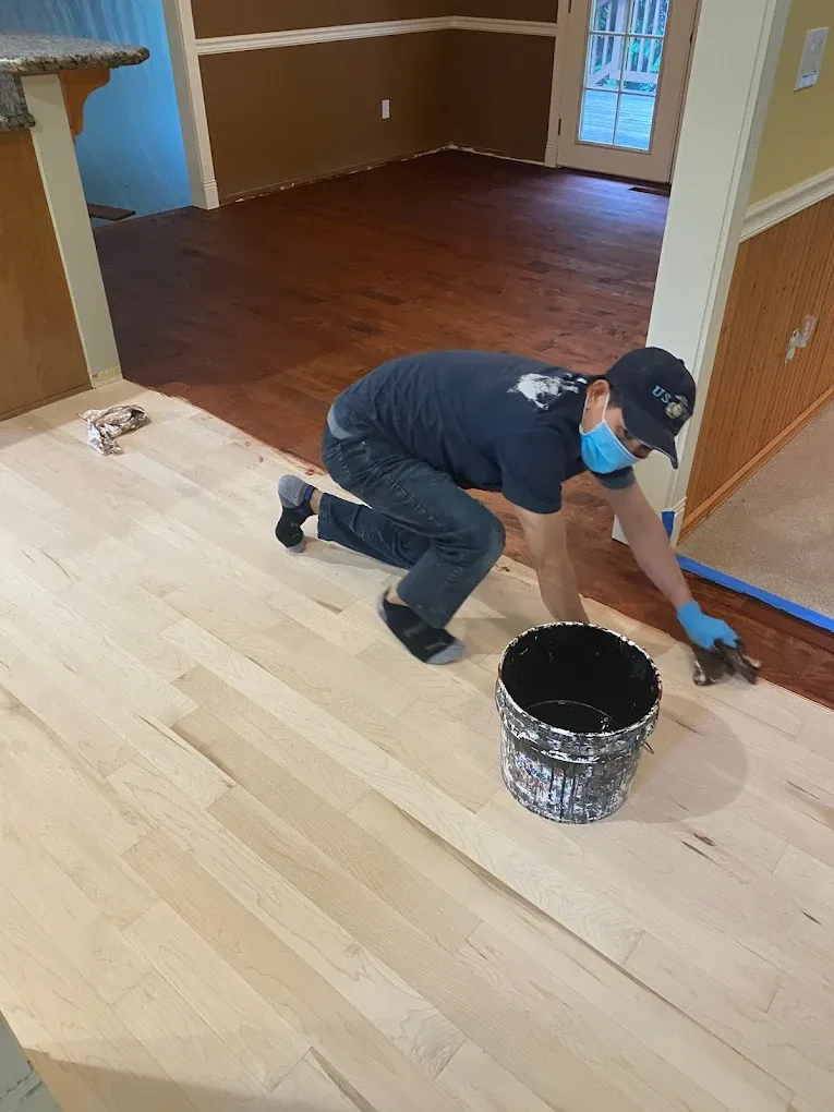 A man is kneeling on the floor painting a wooden floor.