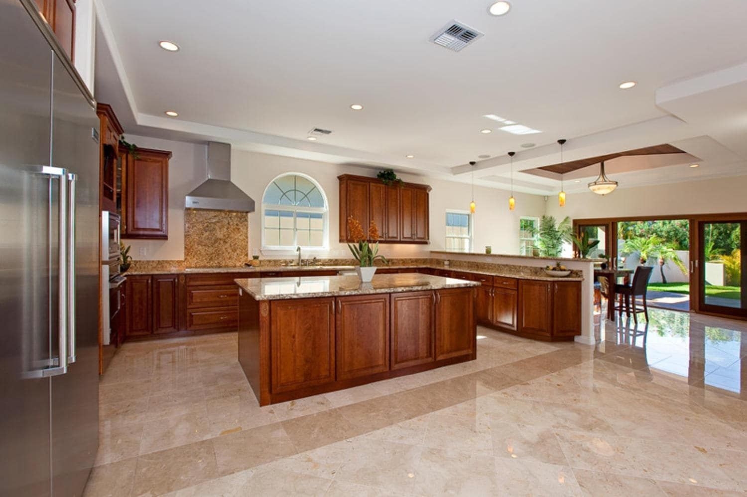 Spacious kitchen with a large island, brown cabinets, granite countertops, and stainless steel appliances.