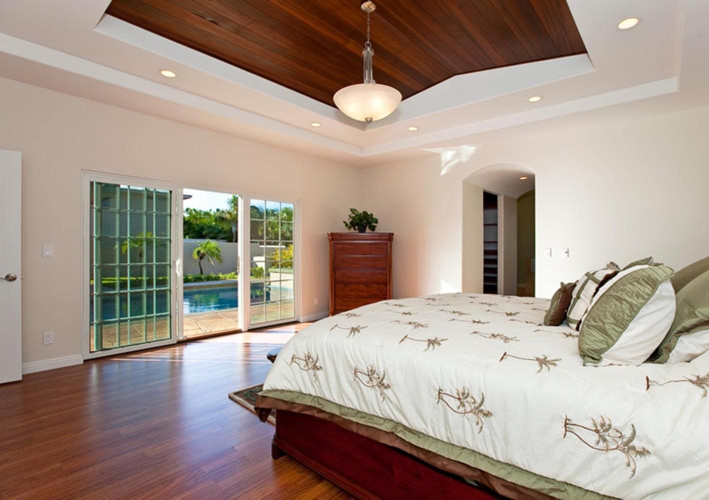 Bedroom with wood ceiling, glass doors to pool, and a large bed with patterned comforter.