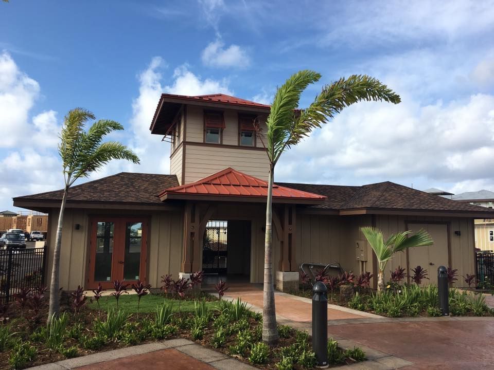 Tan building with red roof, palm trees, and brick walkway under a blue sky.