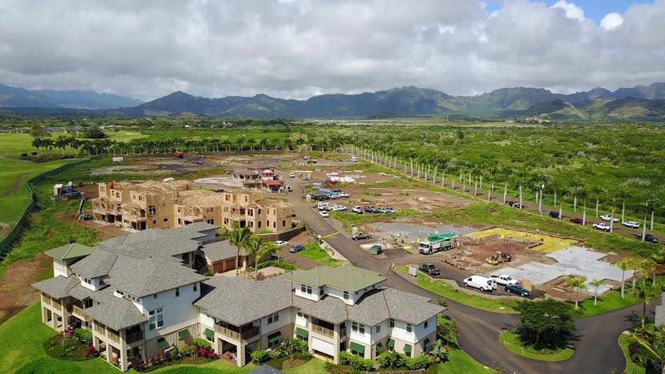 Construction site with new homes, green fields, and mountains under a cloudy sky.