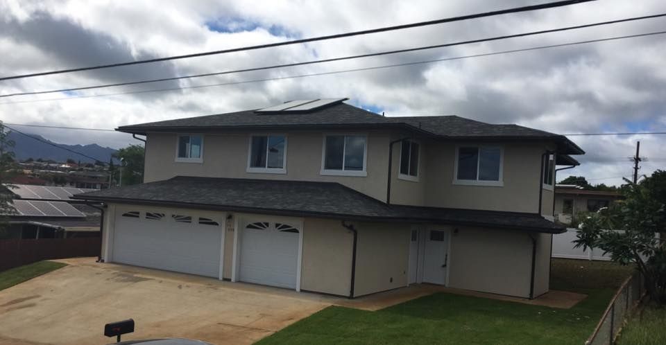 Two-story beige house with two-car garage, dark roof, white trim, and solar panels. Cloudy sky.