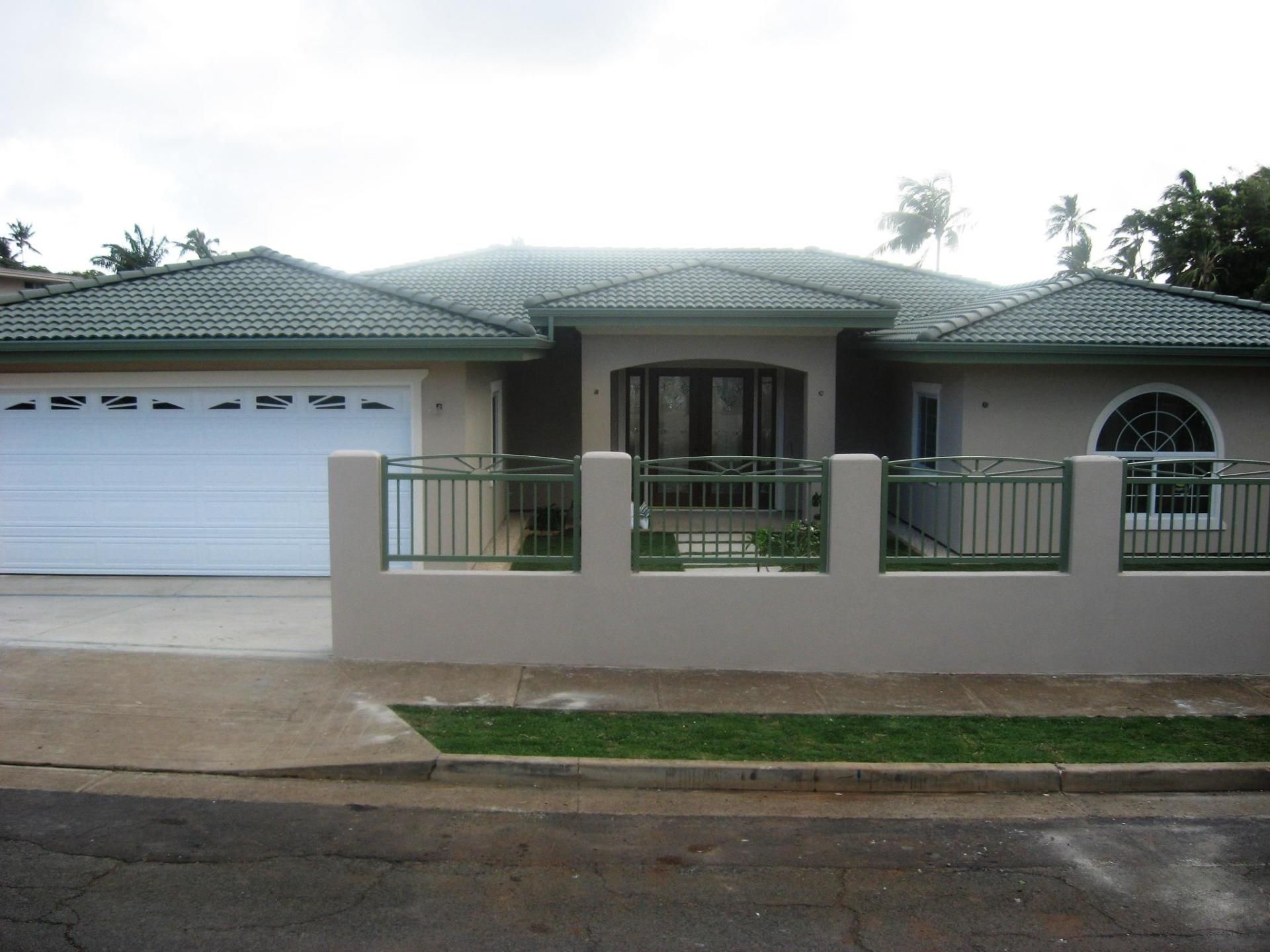 Tan house with green roof and fence; driveway and grass in front.