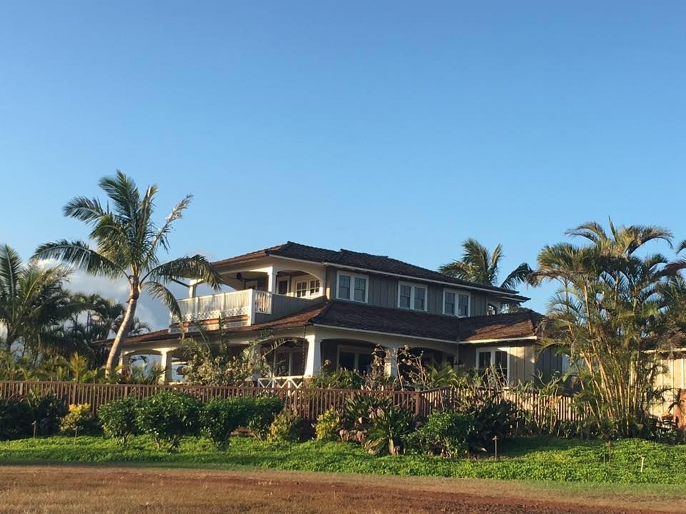 Large two-story house with a wrap-around porch and palm trees against a blue sky.