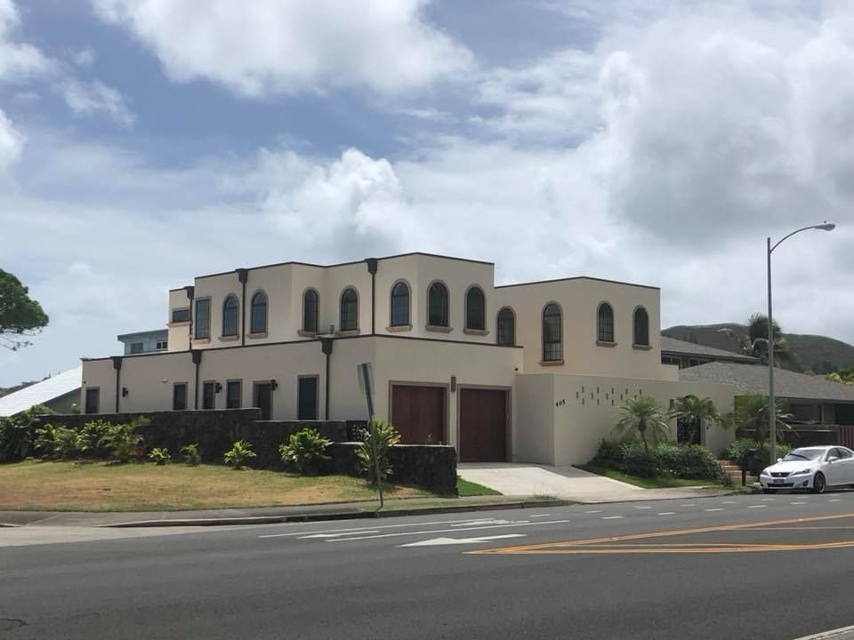 Two-story beige building with arched windows, brown garage doors, and a street in front under a cloudy sky.