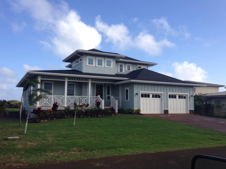 Light blue house with white trim, porch, and two-car garage. Green lawn, blue sky, and clouds in the background.