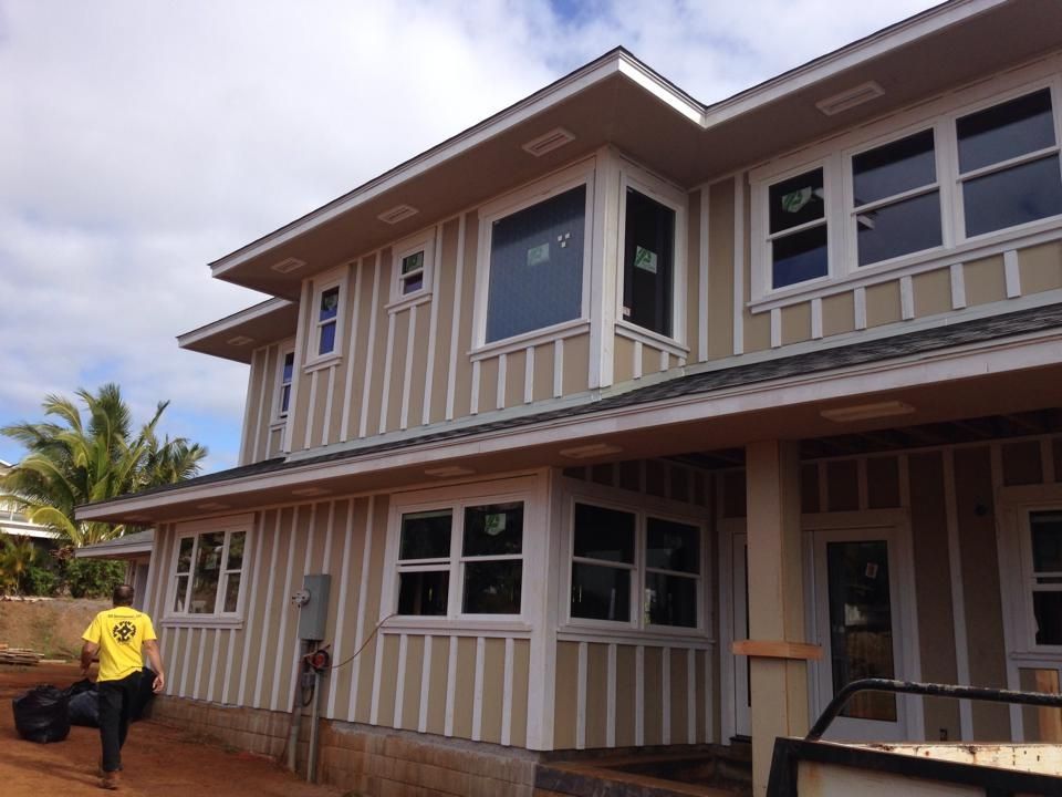 Two-story house with tan siding, white trim. A person walks by with a bag. Sunny day.