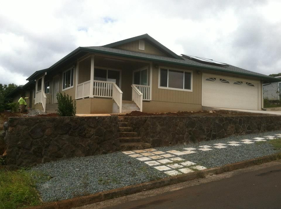 Tan house with a garage, stone retaining wall, and steps leading to the front porch. Cloudy sky.
