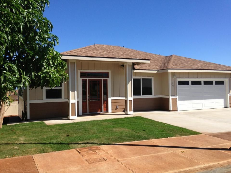 Tan and brown house with a garage, front door, and windows against a clear blue sky.