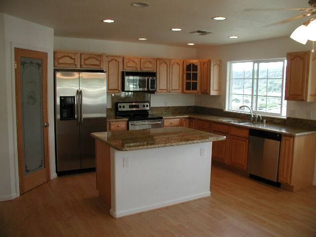 Kitchen with light wood cabinets, stainless steel appliances, and an island with a granite countertop.
