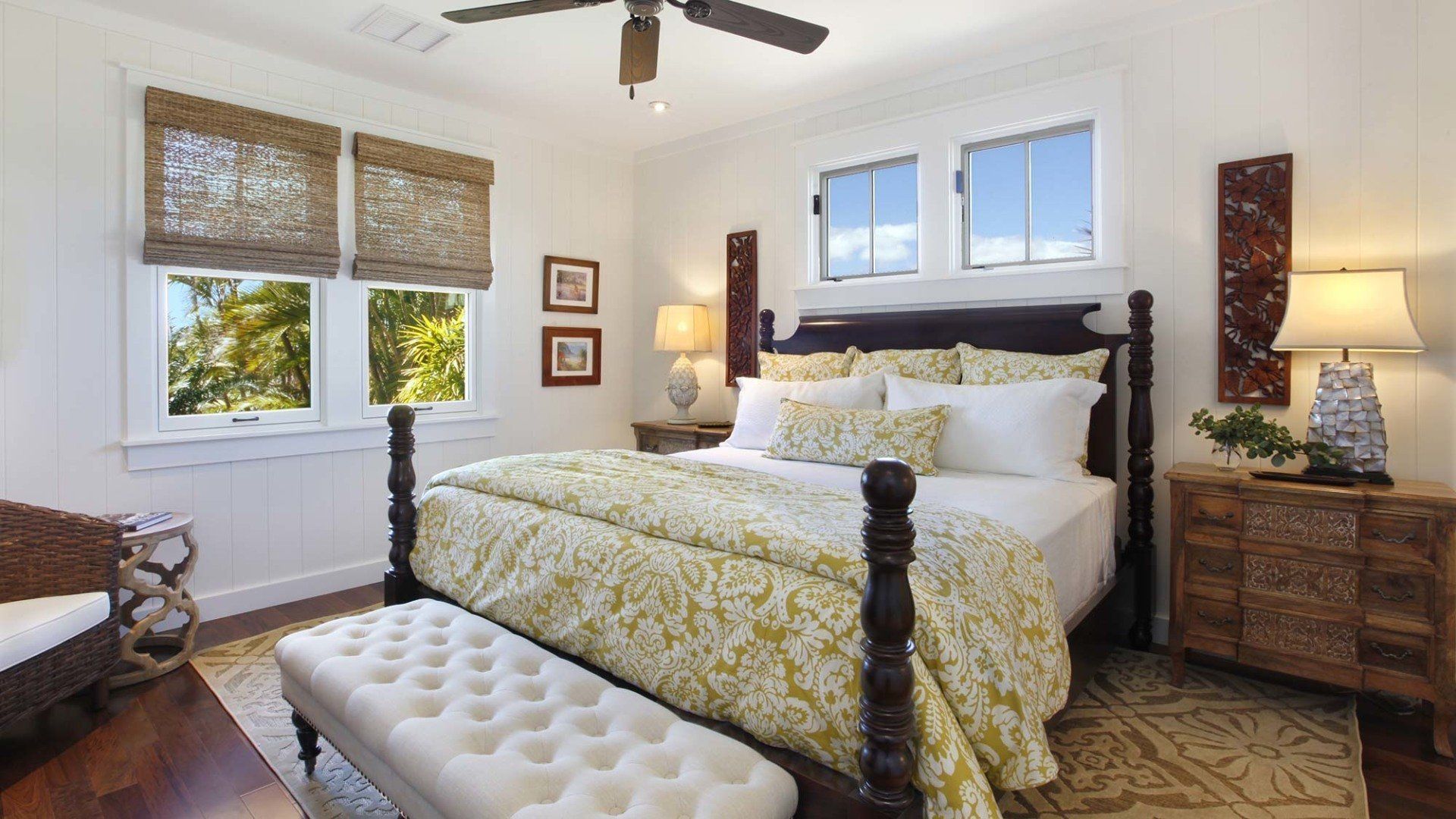 Bedroom with a four-poster bed, windows with woven shades, and a patterned comforter; light and airy design.