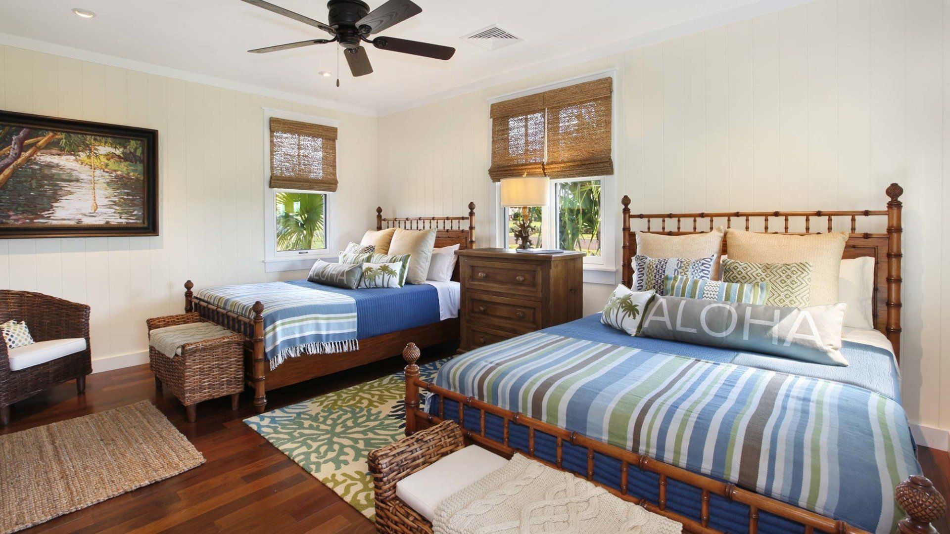 Bedroom with two beds, bamboo frames, blue and green bedding, wicker furniture, and a ceiling fan.