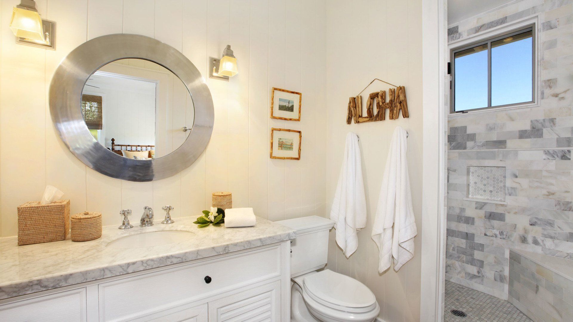 Bathroom with white walls, marble countertops, and a gray tile shower. Contains a round mirror, toilet, and