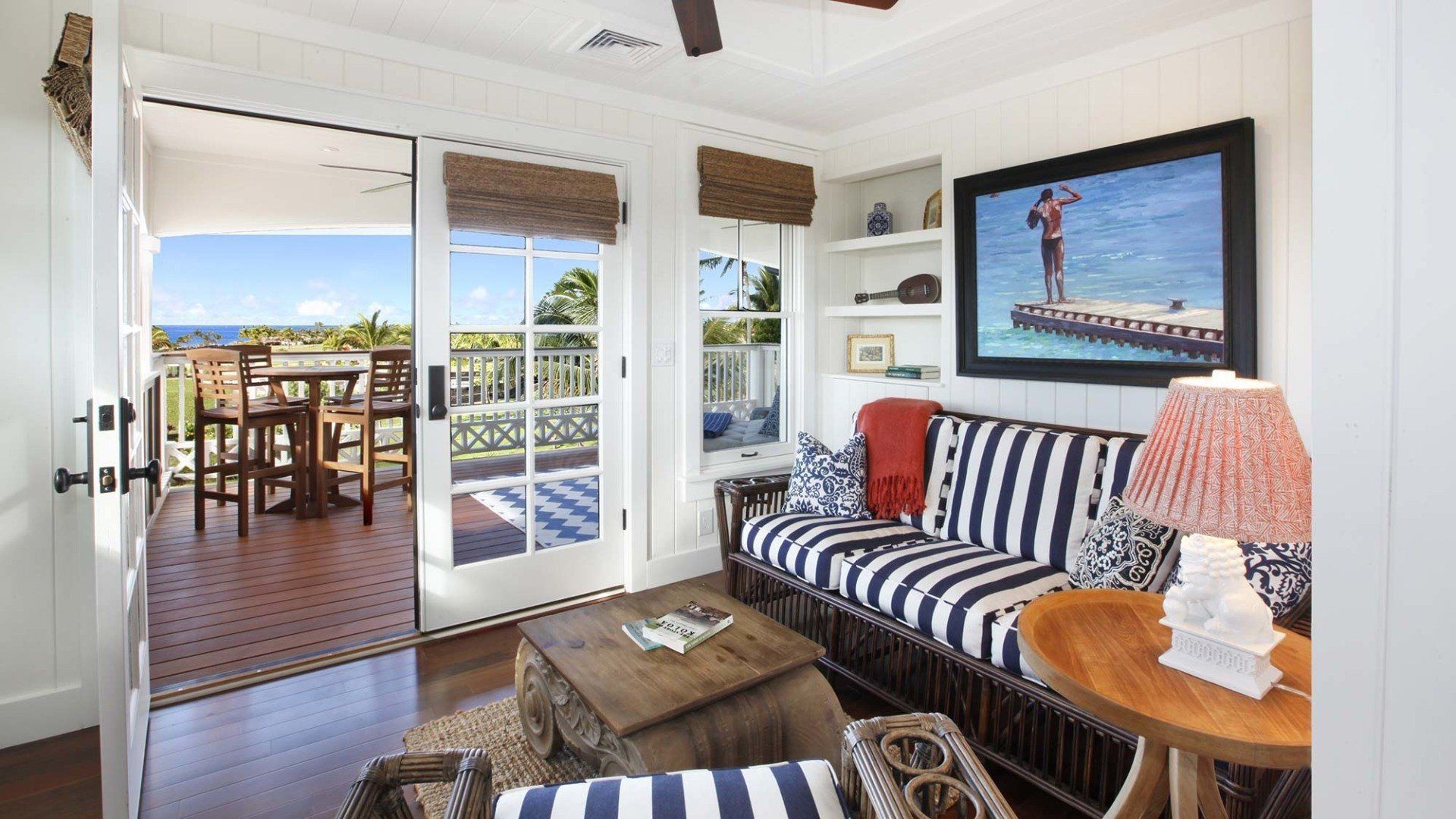 Room with blue and white striped sofa, opening onto a balcony with ocean view.