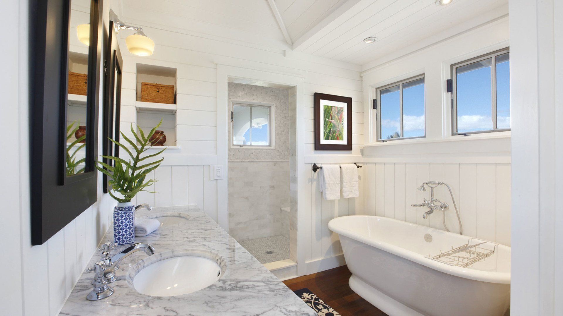 White bathroom with marble countertop, clawfoot tub, and small windows with blue sky view.