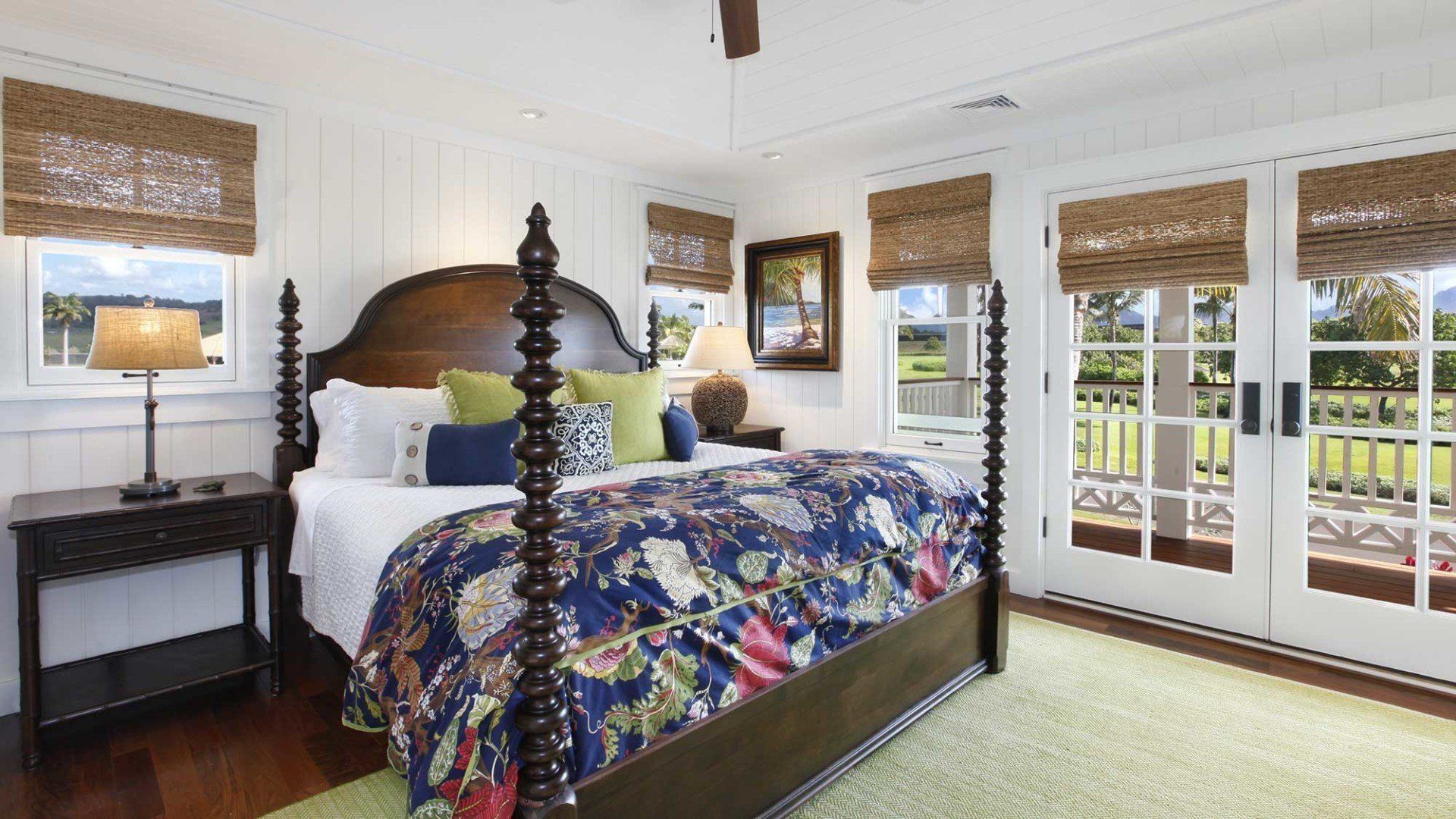 Bedroom with a four-poster bed, patterned bedding, and woven shades. French doors open to a grassy area.