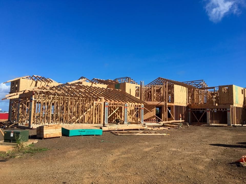Wood frame of a multi-section house under construction against a clear blue sky.