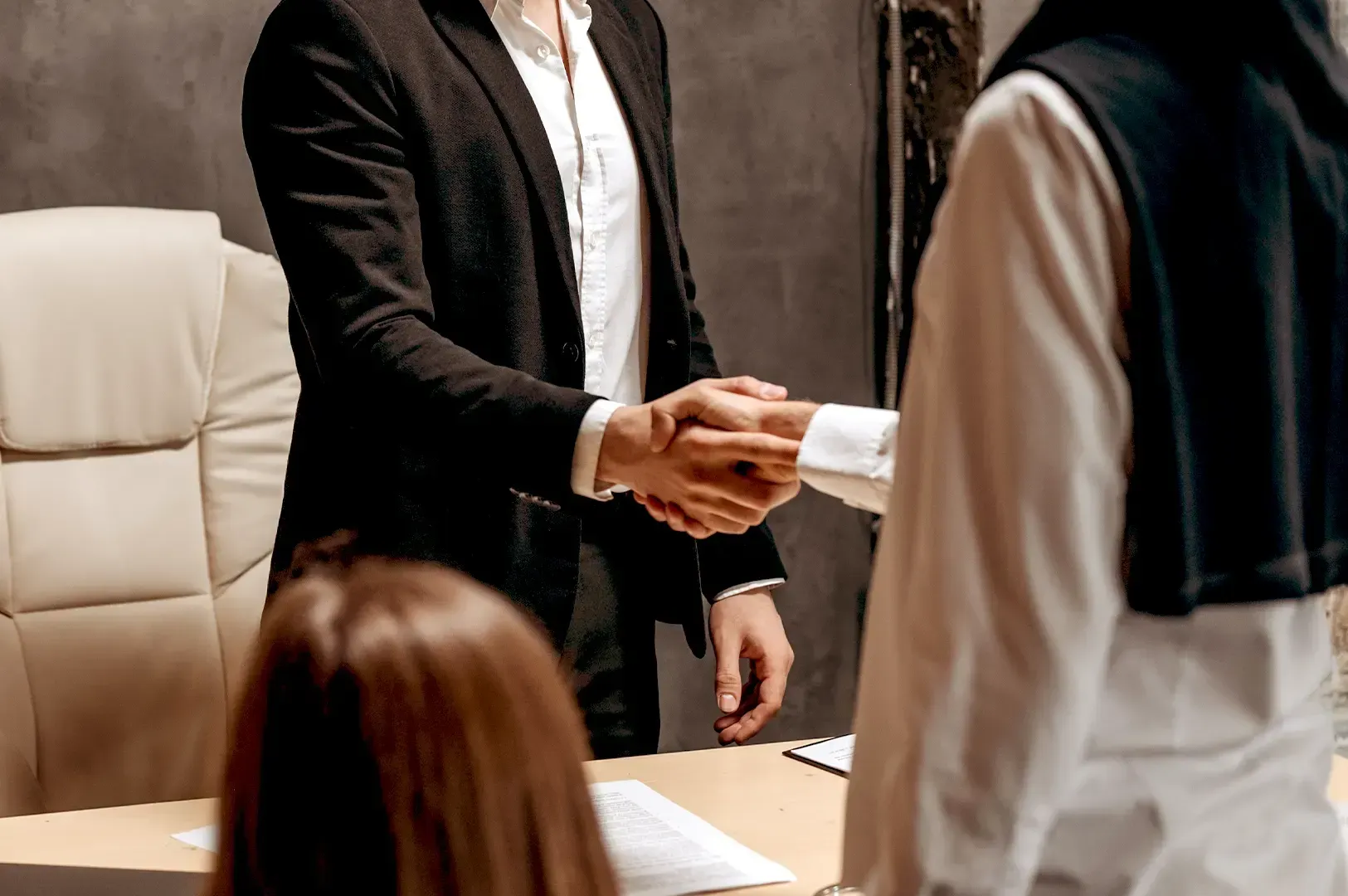 Two business professionals shaking hands across a desk, symbolizing trust, agreement, and the slow,