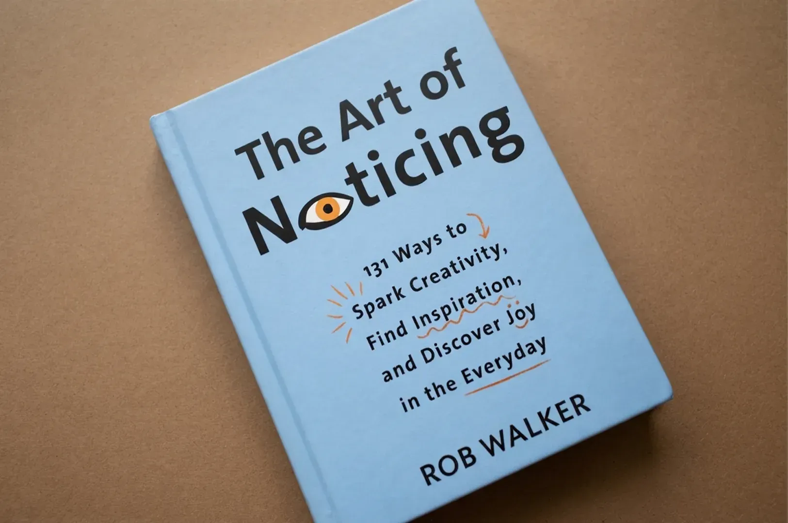 A light blue hardcover copy of The Art of Noticing by Rob Walker resting on a brown surface, highlig