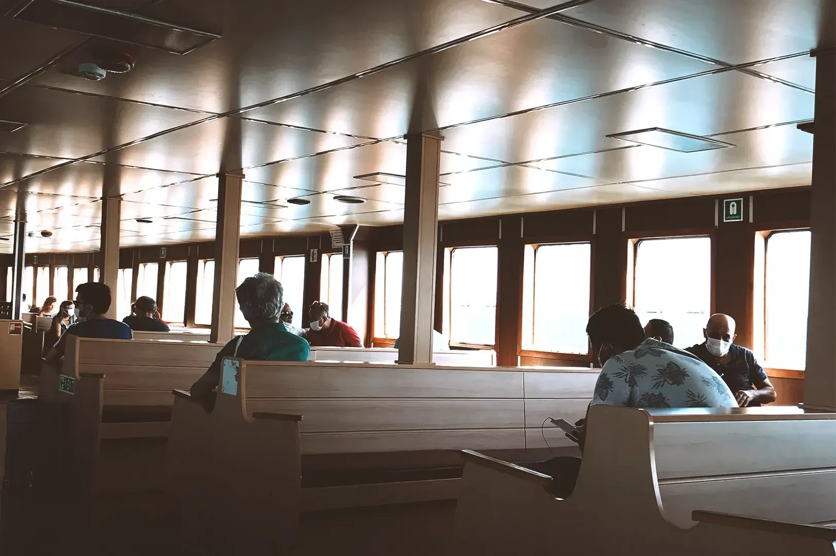 Passengers sitting inside a ferry cabin with rows of wooden benches, capturing a moment of travel in