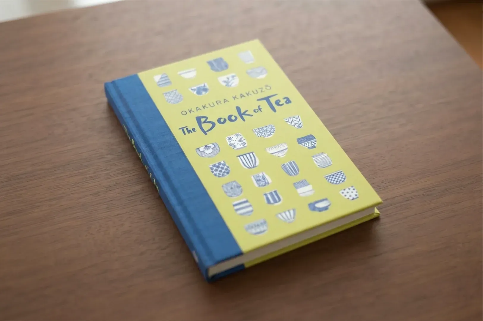 A hardcover copy of The Book of Tea by Kakuzō Okakura resting on a wooden surface, illustrating the